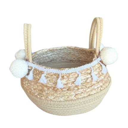 Woven straw basket with two handles and white tassel trim along the rim, decorative pom-poms on the sides.
