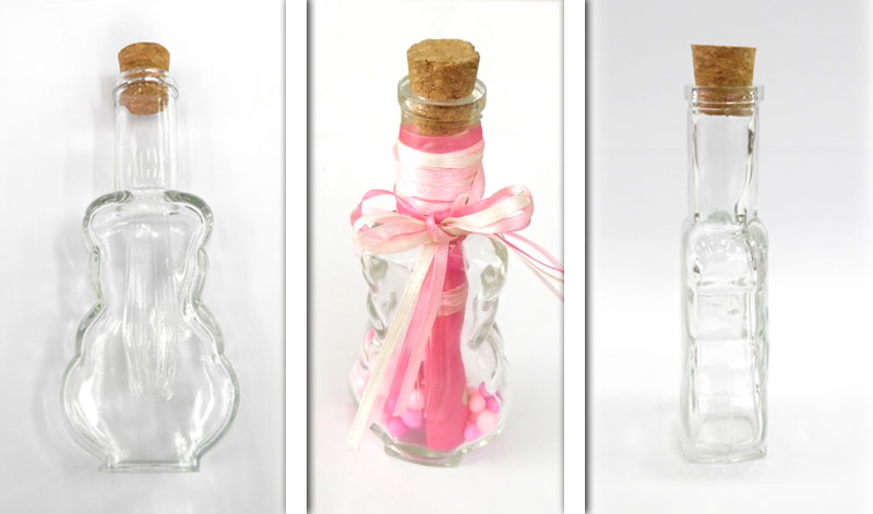 05030261 | La Vie en Rose Three clear glass bottles with corks arranged in a row: a plain irregularly shaped bottle left, a center decorative bottle with pink ribbons and beads, and a tall rectangular bottle right.
