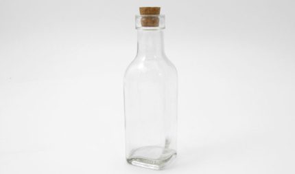 Clear glass bottle with a cork stopper on a white background, empty inside.