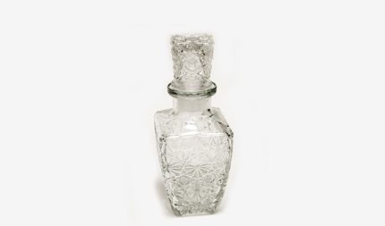 Crystal perfume bottle with an ornate stopper and faceted body on a white background.