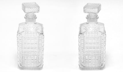 Two clear glass bottles with a grid texture and crystal square stoppers stand side by side against a white background.