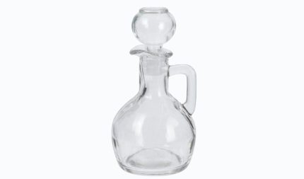 Clear glass decanter with round stopper and short handle, empty in a bright setting.