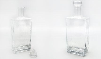 Two empty glass bottles with stoppers on a white background, one cap removed and resting nearby on the left.