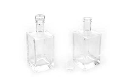 Two empty square glass bottles with stoppers on a white background; stopper removed from the middle foreground bottle.