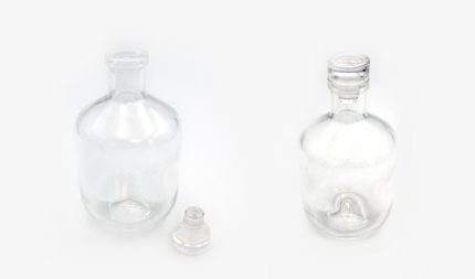 Two empty clear glass bottles with stoppers on a white background