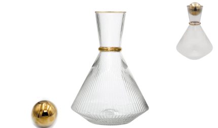 Ribbed clear glass decanter with a stopper and gold band, accompanied by a small gold ball ornament.