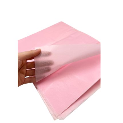 Pink tissue paper being peeled back to reveal a translucent sheet held by a hand, suggesting packaging or craft use.