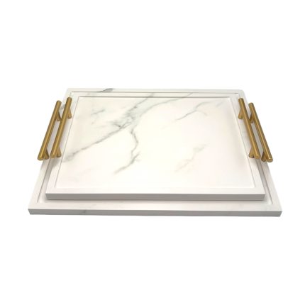 Rectangular white marble cutting board with gold metal handles, stacked on a larger white board against a plain background.
