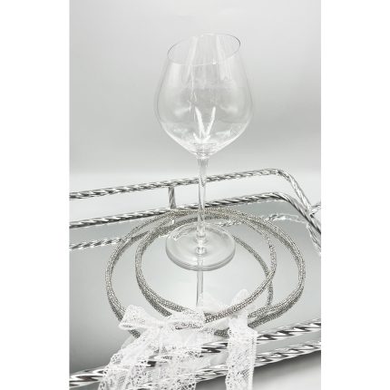 Clear wine glass on a mirrored surface with coiled silver bangles and white lace.