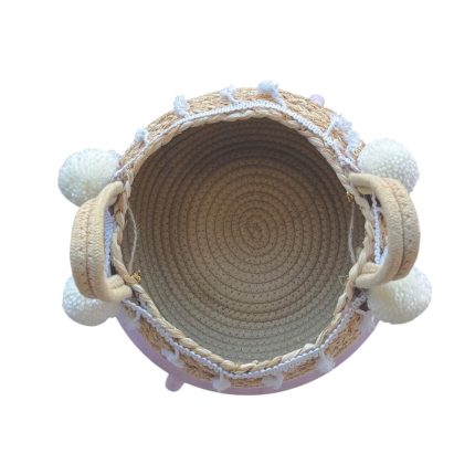 Top-down view of a round woven straw bag with braided rim, white pom-poms on the sides, and short handles.