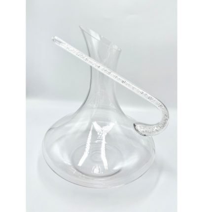 Clear glass decanter with a long, curved crystal-studded handle resting on a white surface, empty and transparent.