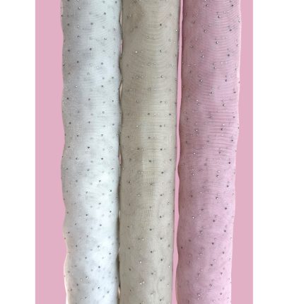Three rolled pastel fabrics (blue, beige, pink) with small bead-like embellishments against a pink background.