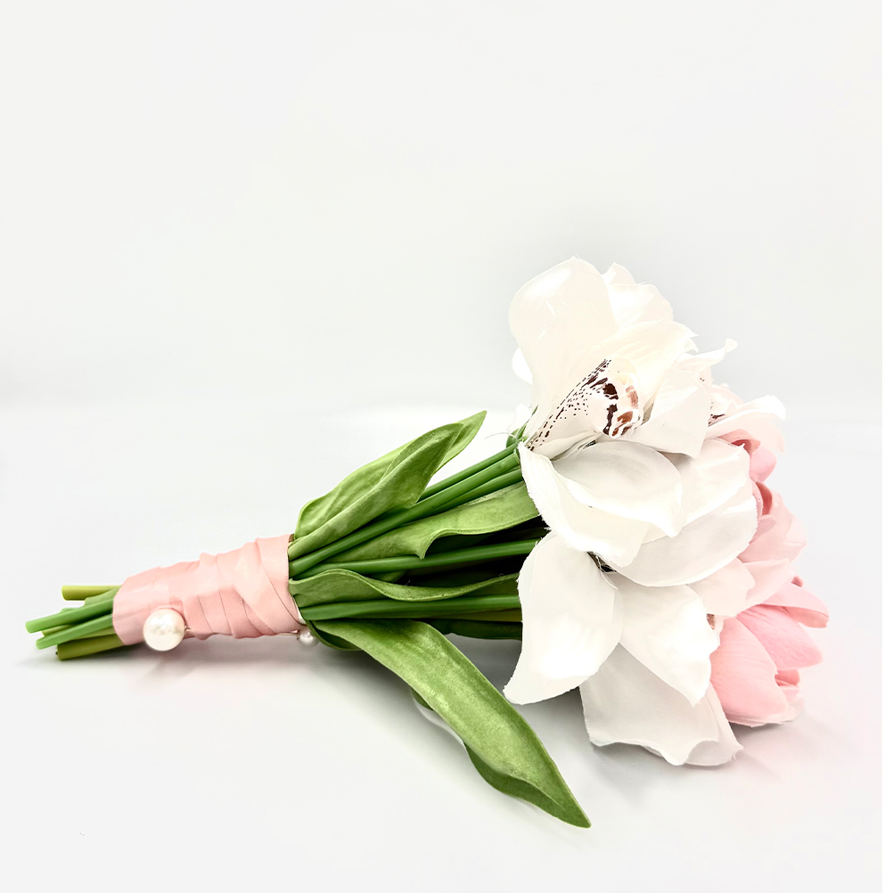 EBEB313D-1829-4DD4-CF2F-019C9A4AA96A_11 | La Vie en Rose White and pale pink bouquet bound with a pink ribbon and a pearl pin, resting on a white surface